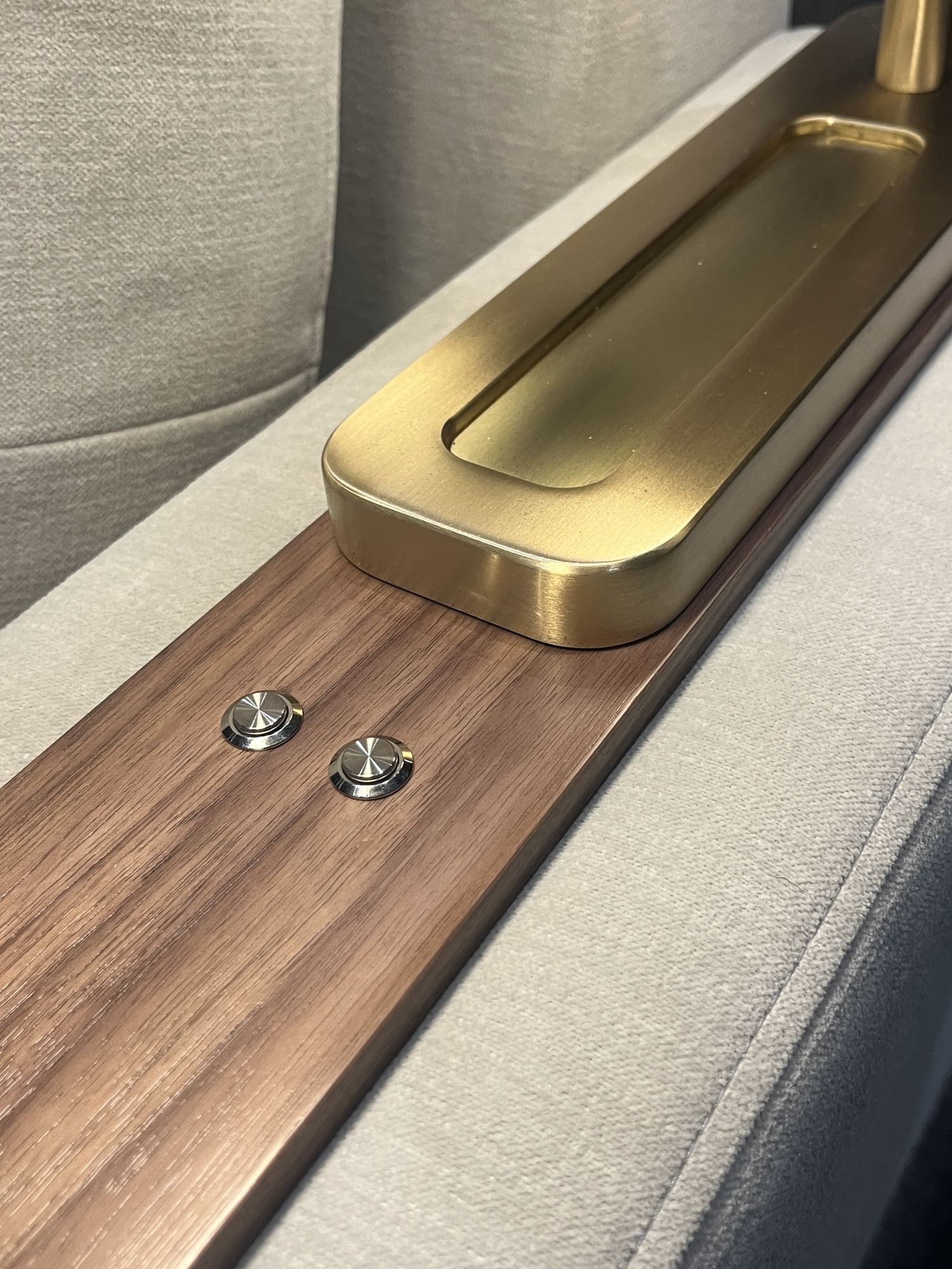 Close detail of the walnut armrest with a brushed-brass inset tray and two machined control buttons set into the timber