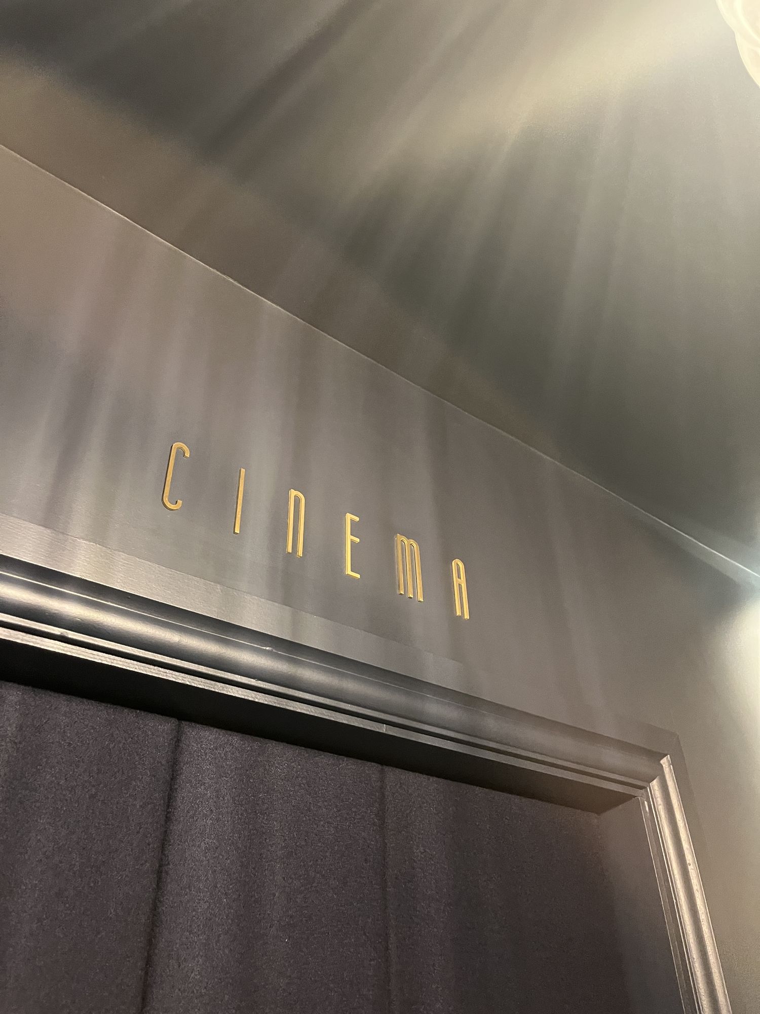 Brass CINEMA lettering set above the padded entrance door to the auditorium